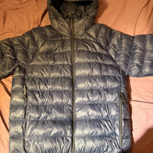 Mörkblå Peak Performance pufferjacka med huva - Säljer en snygg mörkblå pufferjacka med huva. Jackan har en dragkedja framtill och två sidofickor med dragkedjor. Perfekt för kyliga dagar. 