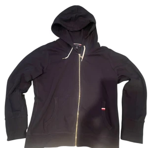 Mörkblå Tommy Hilfiger Zip - Säljer en stilren mörk blå hoodie med dragkedja och huva. Tröjan har långa ärmar och praktiska fickor framtill. Perfekt för en avslappnad look.