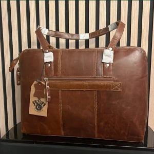 Brun skinnportfölj från C.A.B Sweden - Snygg brun portfölj i äkta skinn från C.A.B Sweden. Väskan har en dragkedja och robusta handtag, perfekt för att bära dina viktiga dokument med stil. Den har en klassisk design med en etikett som visar varumärkets emblem.