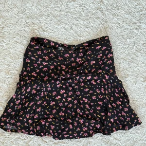 Blommig kortkjol från Zara - Söt blommig kortkjol från Zara. Kjolen är svart med rosa och gula blommor och har en volangdetalj 🌸Inbygda shorts 