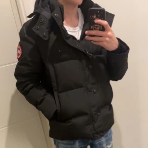 Svart Goose jacka  - Säljer en svart dunjacka från Canada Goose med avtagbar huva och pälsdetalj. Jackan har en klassisk pufferdesign med dragkedja och knappar framtill. Jackan är rätt så ny har endast haft den 1-2 vecjor har kvar allt man fick med från den. Diskuterar dessutom pris men helst något rimligt för jackan är i mycket bra skick 