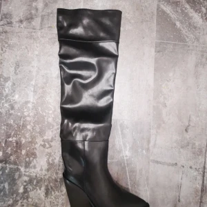 Över knä cowboy skor - Snygga svarta stövlar i skinn med hög kilklack och spetsig tå. Perfekta för en stilren look. Stövlarna har en elegant design som passar till många tillfällen.