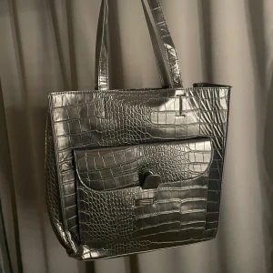 Svart axelväska i krokodilmönster - Svart väska i snake skin-imitation. Rymlig! Får plats med en normalstor dator/laptop. I fint skick!