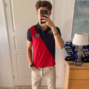 Blå och röd pikétröja från GANT - Säljer en snygg pikétröja från GANT i blått och rött med broderade detaljer och en krage med knappar. Perfekt för en stilren look. 183 cm på bilden!