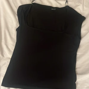 Svart topp från Gina Tricot - Säljer en stilren svart topp från Gina Tricot. Toppen har en enkel design med smala axelband och en bekväm passform. Perfekt för att matcha med olika outfits.