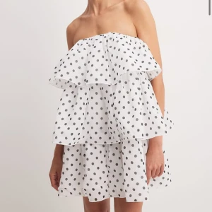 Vit prickig klänning från NA-KD - Säljer en söt vit klänning med svarta prickar från NA-KD. Klänningen är axelbandslös med volanger och har en luftig passform. Perfekt för sommarens varma dagar! Helt ny med lappen kvar, storlek 34. 