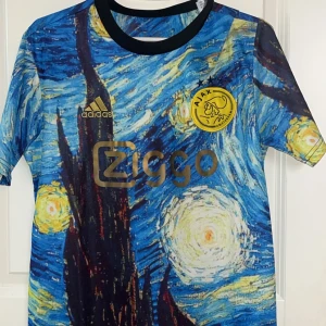 Ajax fotbollströja med Van Gogh-motiv - Unik Ajax fotbollströja från Adidas med ett fantastiskt Van Gogh-motiv. Tröjan har korta ärmar och en färgglad design i blått, gult och svart. Perfekt för samlare eller fans av både fotboll och konst.
