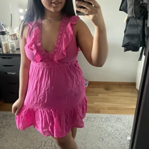 Rosa klänning med volangdetaljer - Söt rosa klänning med volangdetaljer och spets vid halsringningen. Är ärmlös och har knytning i ryggen. Endast använd ett fåtal gånger.