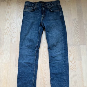 Nudie Gritty Jackson Jeans  - Snygga blå jeansbyxor med klassisk femficksdesign och knappgylf. Perfekta för en avslappnad stil. De har en rak passform och är tillverkade i slitstarkt denim. Storlek W30 L32