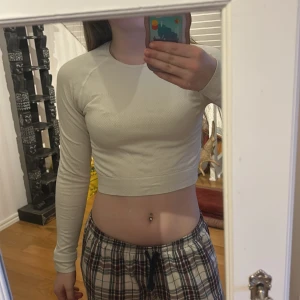 Beige långärmad croppad träningströja  - Säljer en beige långärmad croppad träningströja med rund halsringning. Tröjan har en tight passform och är perfekt för alla sorts träning.