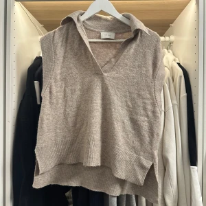 Beige stickad väst från Neo Noir - Beige stickad väst från Neo Noir med krage och v-ringning. Modellen är loose fit med ribbade kanter och slitsar i sidorna. Materialmix av akryl, ull, nylon och elastan ger en mjuk och skön känsla. Perfekt att slänga över en t-shirt för en chill look.