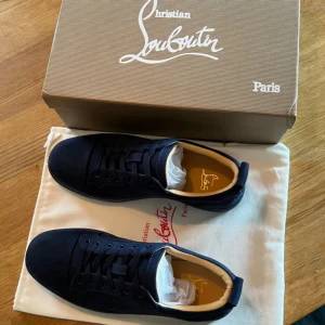 Mörkblå sneakers från Christian Louboutin - Snygga mörkblå sneakers från Christian Louboutin i mocka med klassisk rund tå och platt sula. Skorna har svarta snören och diskret branding på insidan. Perfekta för dig som vill ha en stilren och lyxig look.