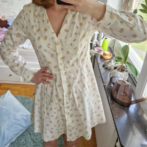 Blommig klänning - Kort, blommig klänning med långa ärmar och spetsdetaljer på kragen. Aldrig använd!