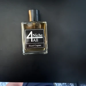 Niche4All  Hazel Cognac parfym - Parfymflaska i glas med svart etikett och svart kork. Doften heter Hazel Cognac och vätskan har en gyllene ton. Flaskan har en stilren, fyrkantig form och känns lyxig och modern.