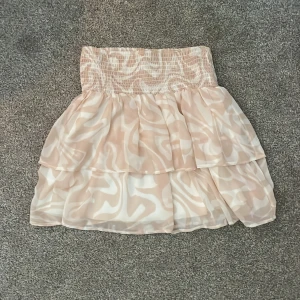 Rosa volangkjol med mönster - Supersöt kort volangkjol i beige och vitt med abstrakt mönster. Kjolen har bred smock i midjan och dubbla lager för extra volym. Priset kan diskuteras!💗