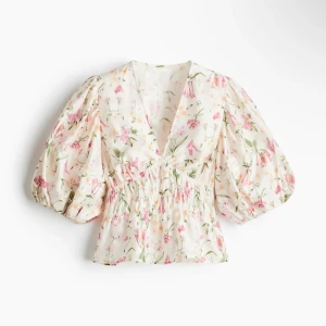 Blommig blus med puffärm och v-ringning - Supersöt blommig blus i vitt med rosa och gröna detaljer. Den har v-ringning, smockad midja och puffiga korta ärmar som ger en romantisk vibe. Perfekt för dig som gillar en feminin och trendig look. Lätt och luftig, passar perfekt till jeans eller kjol.