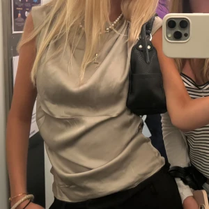 Silvrig/ljusgrön ärmlös linnetopp i satin - Snygg silvrig/grön skimrig linnetopp i satin med draperad halsringning. Toppen är ärmlös och har en lätt glansig finish som ger en lyxig känsla. ❤️