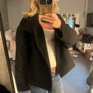 Svart kappa  - Säljer en svart kappa med bred krage och dubbelknäppning. Jackan har en boxig passform och är tillverkad i ett tjockare material som känns lyxigt. Perfekt för dig som gillar en stilren och klassisk look med en modern twist. 