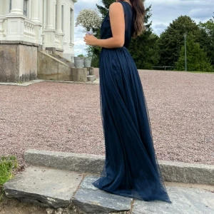 Marinblå balklänning oneshoulder  - Säljer en elegant marinblå långklänning i luftig mesh med oneshoulder och transparent tyg upptill. Klänningen har markerad midja och ett svepande fall som ger en riktigt snygg siluett. Perfekt för bal eller student!