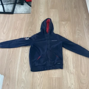 Marinblå fleecejacka race marine - Marinblå fleecejacka från race marine ta med röd insida på huvan och detaljer vid fickorna. Jackan har dragkedja hela vägen, två fickor fram och broderad logga på bröstet samt ärmen. Perfekt för kyliga dagar och snygg till jeans.