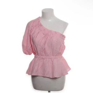 Rosa omlott blus med oneshoulder - Supersöt rosa blus med volangkant och resår i midjan. Toppen har en ärm och en axel är bar för en trendig oneshoulder-look. 💘💘