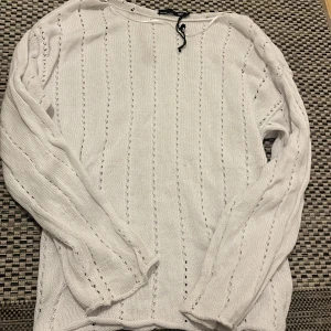 Vit stickad tröja från 157 - Vit stickad tröja från 157 med långärmad design och diskreta hålstickade ränder. Tröjan har en klassisk rund halsringning och är perfekt för lager-på-lager-stil. Mjuk och skön känsla, passar till jeans eller kjol.