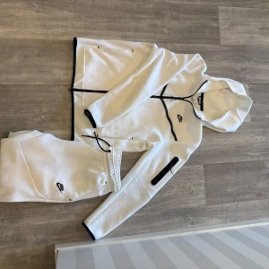 Vit Nike tech fleece set  - Nike tech fleece set i vitt med svarta dragkedjor och detaljer. Jackan har huva, hel dragkedja framtill och en extra ficka på ärmen. Snygg sportig look med svart Nike-logga på bröstet. Perfekt för chill eller träning. Nike settet har jag aldrig andvänt så skicket är nästintill helt nytt, storlek M.
