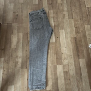 Grå jeans från Woodbird - Säljer ett par grå jeans från Woodbird med klassisk femficksdesign och raka ben. Jeansen har en snygg tvättad look, normal passform och är tillverkade i bomull. Perfekta för dig som gillar stilrena och enkla jeans med en modern vibe. Storlek 30/30
