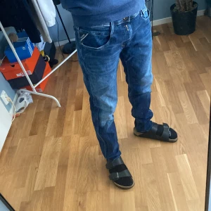 Replay Anbass slim fit jeans blå - Säljer ett par Replay Anbass slim fit jeans i klassisk blå tvätt. Jeansen har fem fickor, snygga slitningar och kontrastsömmar. Modellen är smal och sitter riktigt schysst på benen. Perfekta för dig som gillar en modern och stilren look.