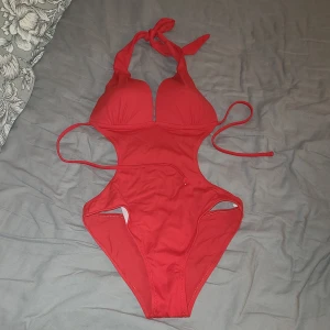 Röd cut-out baddräkt med knyt - Snygg röd baddräkt med cut-out design och vadderade kupor. Halterneck med knyt i nacken och smala knytband i sidorna för en justerbar passform. Står ej storlek eller märke, men passar S. 