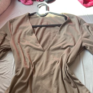 Beige v-ringad body från H&M - Säljer en beige body från H&M i storlek M. Bodyn har lång ärm, djup v-ringning och är figurnära med kort längd. Mjuk och stretchig känsla, perfekt för en clean och stilren look.