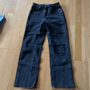 Svarta raka jeans från Zara - Svarta jeans från Zara i rak modell med råa, fransiga benslut. Klassisk femficksdesign och midja som sitter snyggt. Jeansen är tillverkade i ett stadigt denimtyg och passar perfekt till sneakers eller boots.