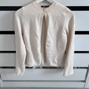 Beige kofta från Gina Tricot - Mysig beige kofta från Gina Tricot med rund halsringning och en knapp upptill. Koftan är stickad i ett mjukt material och har långa ärmar samt ribbade muddar vid hals, ärmslut och nederkant. Perfekt att slänga över en topp för en chill look.