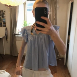 Ljusblå blus med volangärmar Gina Tricot - Supersöt ljusblå blus från Gina Tricot med v-ringning, volangiga korta ärmar och broderade detaljer upptill.