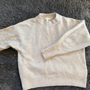 Beige stickad tröja med pärlor H&M - Superfin beige stickad tröja från H&M med små pärldetaljer över hela tröjan. Tröjan har rund halsringning, ribbade muddar och lång ärm. Perfekt för dig som gillar en söt och stilren look.