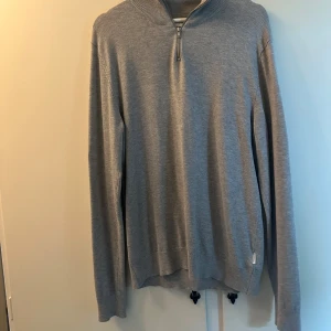 Grå half zip tröja från Lindbergh - Snygg grå långärmad tröja från Lindbergh med half zip-dragkedja vid halsen. Tröjan har en stilren och enkel design med ribbad krage och är tillverkad i mjukt material. Använd fåtal gånger, inga anmärkningar på användning