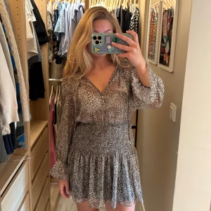 Leopardmönstrad kortklänning från Zara - Supersöt kortklänning från Zara med leopardmönster i beige och bruna toner. Klänningen har långärmade volangärmar, smockad midja och v-ringning med knappar. Tunt, luftigt material som känns lätt och flowy.