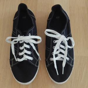 Svarta sneakers  med vita detaljer - Svarta sneakers från H&M med vita snören och kontrasterande vita sömmar.  Dom är knappt använd så i jätte fint skick förutom lite smutsiga under sulorna , se bild. Från rök och djurfritt hem