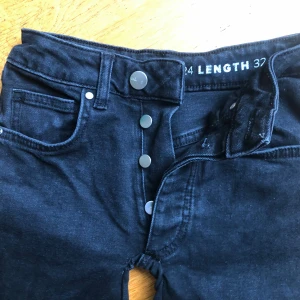 Svarta bootcut jeans från Bik bok w24/L32 - Säljer ett par svarta bootcut jeans från Bik bok med klassisk femficksdesign och knappgylf. Jeansen är tillverkade i stretchig denim (98% bomull, 2% elastan) och har en snygg passform med utsvängda ben. Det finns ett litet hål i grenen men tyget är du dubbelt där så huden lyser inte igenom. Lätt att sy igen. Perfekta för dig som gillar en tidlös look. Rök och djurfritt hem.