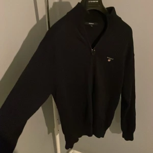 Svart half zip tröja från GANT - Svart långärmad tröja från GANT i storlek M med half zip och liten logga på bröstet. Tröjan har en klassisk, normal passform och är tillverkad i mjukt stickat material. Perfekt för dig som gillar stilrena och enkla plagg med diskret branding. Hör av er vid funderingar🤗