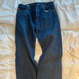 Levi's 501 mörkblå jeans W32 L32 - Klassiska Levi's 501 jeans i mörkblå tvätt med raka ben och fem fickor. Jeansen har knappgylf och är tillverkade i slitstarkt bomullsjeansmaterial. Perfekt för dig som gillar tidlös stil och vill ha ett par snygga jeans med autentisk känsla.