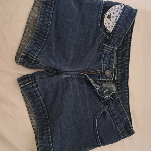 Mörkblåa Jeansshorts  - Fina jeansshorts med detaljer på bakfickorna. Medellånga ben men low waisted. Köpt från en marknad i Thailand.