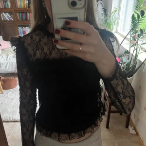 Svart spetsblus från Noisy May - Supersnygg svart blus från Noisy May i transparent spets med lång ärm och volangdetaljer. Blusen har en croppad passform, dragkedja i ryggen och coola spetsmönster över hela plagget. Perfekt för dig som gillar statement-plagg och vill sticka ut. #stockholmstyle #trendy #summer #blus