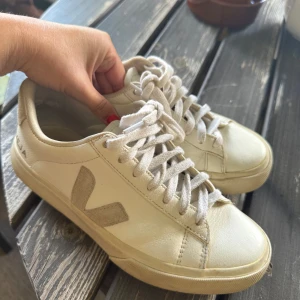 Vita Veja skor - Snygga vita sneakers från Veja med klassisk låg profil och rund tå. Skorna har en beige mockadetalj i form av ett V på sidan och vita snören. Perfekta för dig som gillar minimalistisk stil. Nypris är 1785kr! Använd få gånger.