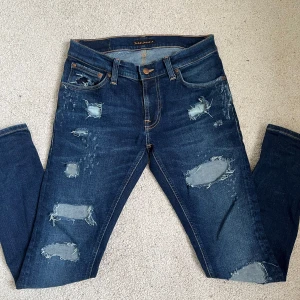Nudie jeans - Säljer ett par mörkblå jeans från Nudie Jeans med riktigt snygga slitningar framtill. Jeansen har klassisk femficksdesign, orange sömmar och är tillverkade i jeansmaterial. Perfekt för dig som gillar en edgy och avslappnad stil. Dom är i storlek 29/30 men jag skulle säga att dom passar bättre som 29/32. (Man ser ingen hud)