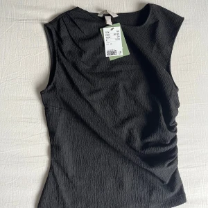 Svart topp från H&M - Svart topp från H&M i storlek XS med strukturerat tyg. Så snygg modell och helt ny! Nypris: 99kr☺️