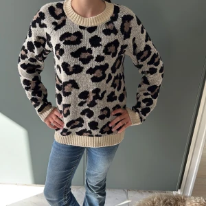 Beige leopardmönstrad stickad tröja - Säljer en beige stickad tröja från KIDSONLY med leopardmönster i svart och brunt. Tröjan har rund hals, ribbade muddar och lång ärm. Perfekt för dig som gillar djurmönster och vill ha en mysig och cool look.