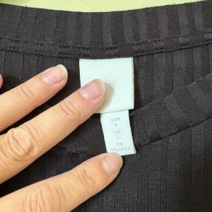 Svart ribbad t-shirt från H&M - Svart t-shirt från H&M i storlek L med ribbad struktur och raka linjer. Modellen är loose fit med korta ärmar och rund halsringning. Perfekt för dig som gillar enkel och stilren design med lite extra textur.