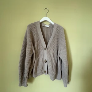 Beige stickad kofta från H&M XL - Säljer en beige stickad kofta från H&M i storlek XL. Koftan har grov ribbstickning, v-ringad hals och tre stora knappar framtill. Perfekt för lager-på-lager och chill stil. 