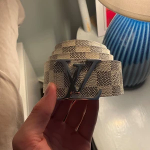  rutig skin bälte  - Snyggt rutig bälte i beige och vit skinn med silver på spännet. Perfekt för att lyfta din outfit med en lyxig touch och klassisk design. Bältet har ett stilrent mönster och känns riktigt exklusivt.